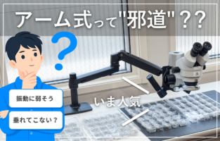 Cartoon man thinking beside a lab bench with a robotic-arm microscope over a grid of samples; speech bubbles say 'Vibration sensitive?' and 'Will it sag?', with a banner noting 'Is arm-style popular?'