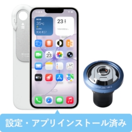 Smartphone with home screen visible and a clip-on blue camera lens attached to the right; white case behind, blue banner at bottom with Japanese text meaning 'Settings and apps installed'